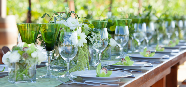 table setting with green wine glasses, white plates and orchids